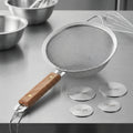 Metal kitchen strainer with fine holes and an elegant wooden handle